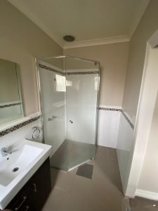 Before photo of the Coburg bathroom renovation showing original corner shower, white vanity and tiled walls
