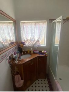 Before photo of the Blackburn bathroom renovation showing original wooden vanity, patterned floor tiles and lace curtains